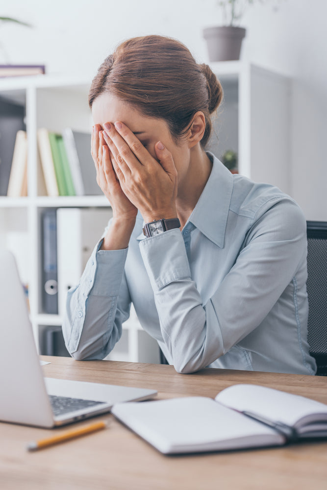 Stressed adult businesswoman covering face with hands at office desk